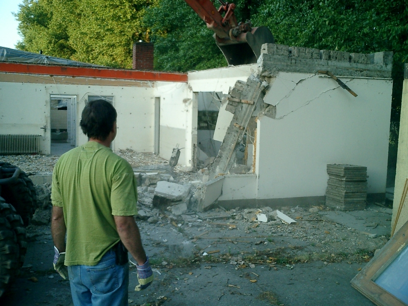 Das alte Vereinsheim fällt
19. Juli 2003, 6.00 Uhr MESZ. Jetzt ist es soweit. Nach komplettem Ausbeinen des alten Vereinsheimes und dem Rückbau des Flachdaches rückt der Bagger den verbliebenen Mauern zu Leibe.
